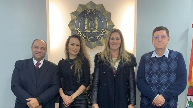 Autoridades posam para foto, em pé, em frente ao brasão da Polícia Civil do RS, fixado na parede ao fundo