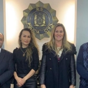 Autoridades posam para foto, em pé, em frente ao brasão da Polícia Civil do RS, fixado na parede ao fundo